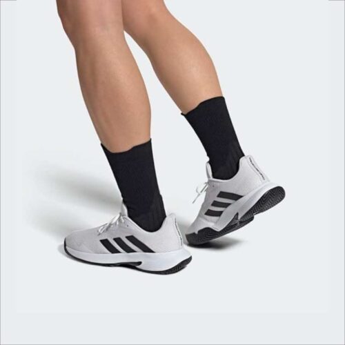 Person wearing white Adidas CourtJam Control padel shoes with black stripes, shown from the side during movement.